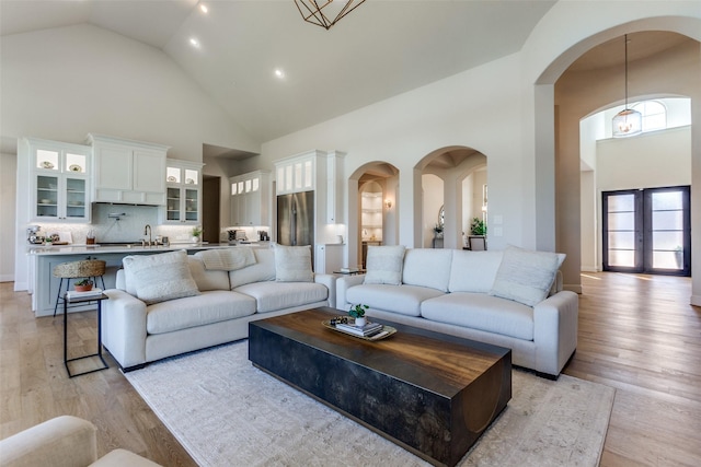 living area with light wood-type flooring, arched walkways, and high vaulted ceiling