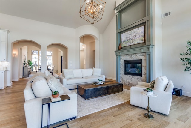 living area with visible vents, light wood-style flooring, arched walkways, a premium fireplace, and a towering ceiling