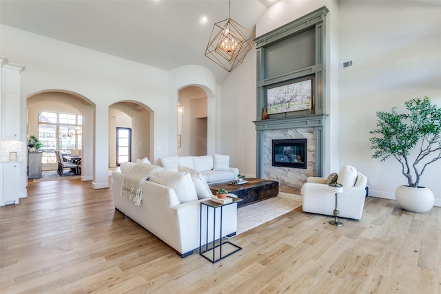 living area with a fireplace, a high ceiling, light wood-style floors, and arched walkways