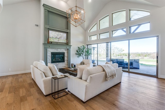 living area with visible vents, a premium fireplace, light wood-style flooring, a notable chandelier, and high vaulted ceiling