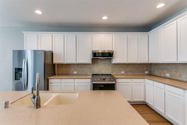 kitchen with appliances with stainless steel finishes, white cabinetry, a sink, and backsplash