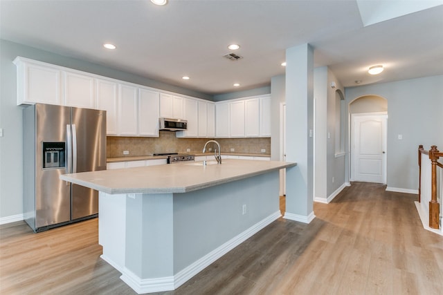 kitchen featuring tasteful backsplash, arched walkways, light wood-style flooring, appliances with stainless steel finishes, and light countertops