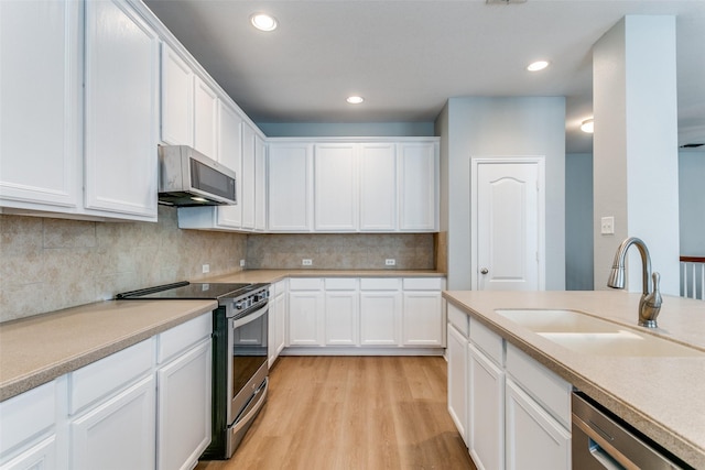 kitchen with light wood finished floors, white cabinetry, stainless steel appliances, and a sink