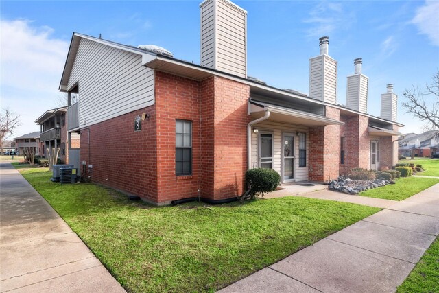 view of side of property with brick siding, a lawn, a chimney, and central air condition unit