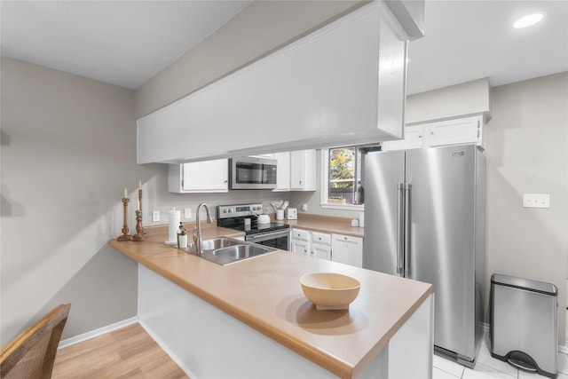 kitchen with stainless steel appliances, a peninsula, a sink, and white cabinets