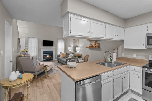 kitchen with appliances with stainless steel finishes, a peninsula, a lit fireplace, white cabinetry, and a sink