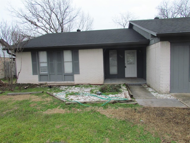 entrance to property with brick siding, a lawn, and a shingled roof