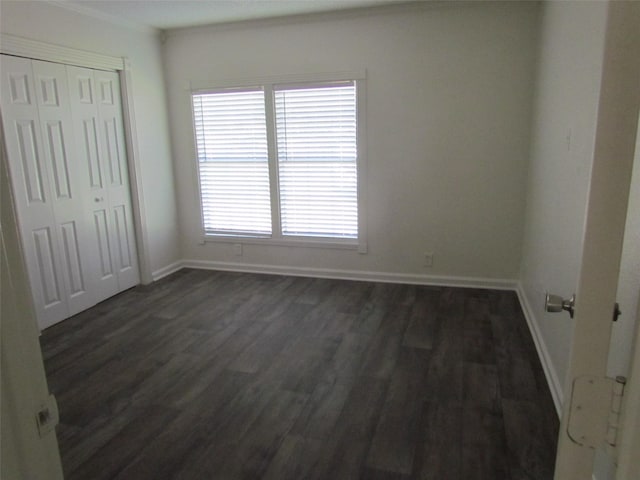 unfurnished bedroom featuring a closet, baseboards, dark wood-type flooring, and ornamental molding