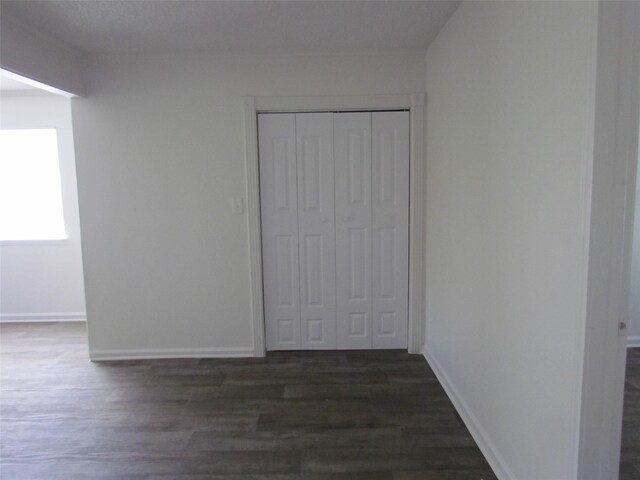 unfurnished bedroom with dark wood-type flooring, a closet, and baseboards