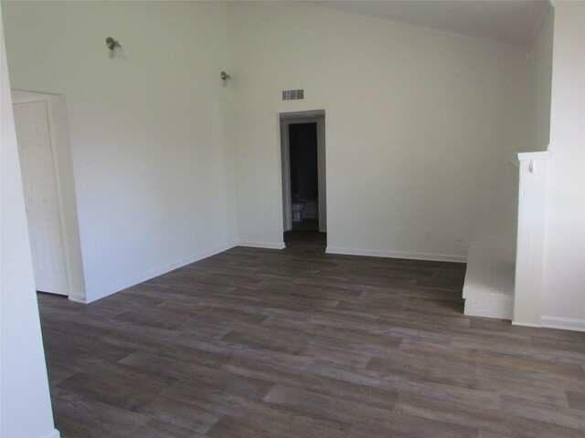 empty room featuring high vaulted ceiling, dark wood-style flooring, visible vents, and baseboards