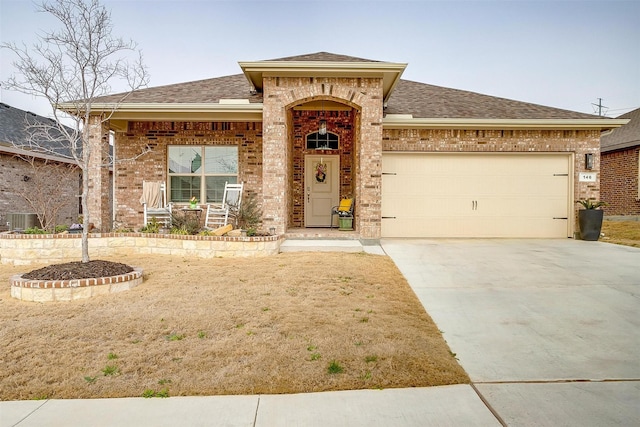 view of front of home featuring central AC unit, a garage, brick siding, a shingled roof, and driveway