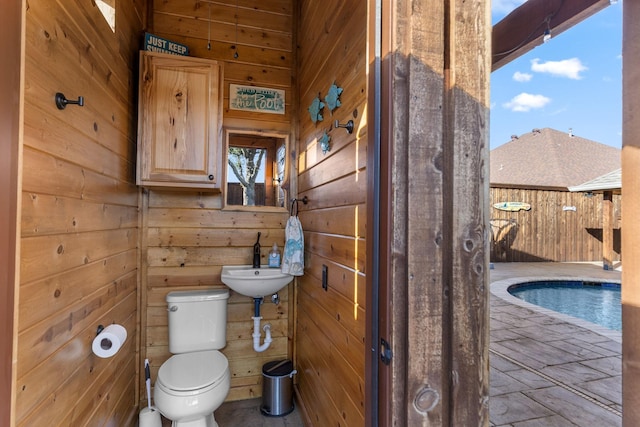 half bathroom with a sink, wood walls, and toilet