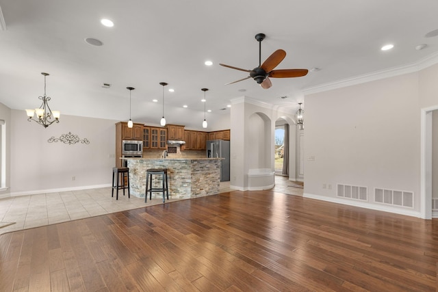 unfurnished living room featuring arched walkways, visible vents, light wood finished floors, and ceiling fan with notable chandelier