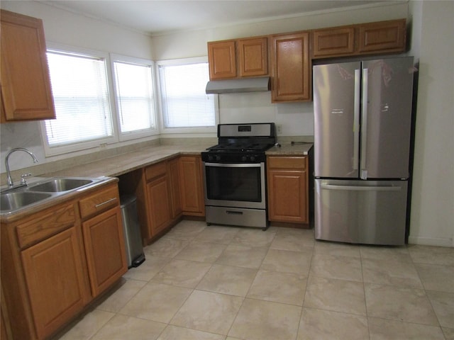 kitchen featuring light tile patterned floors, appliances with stainless steel finishes, brown cabinetry, a sink, and under cabinet range hood