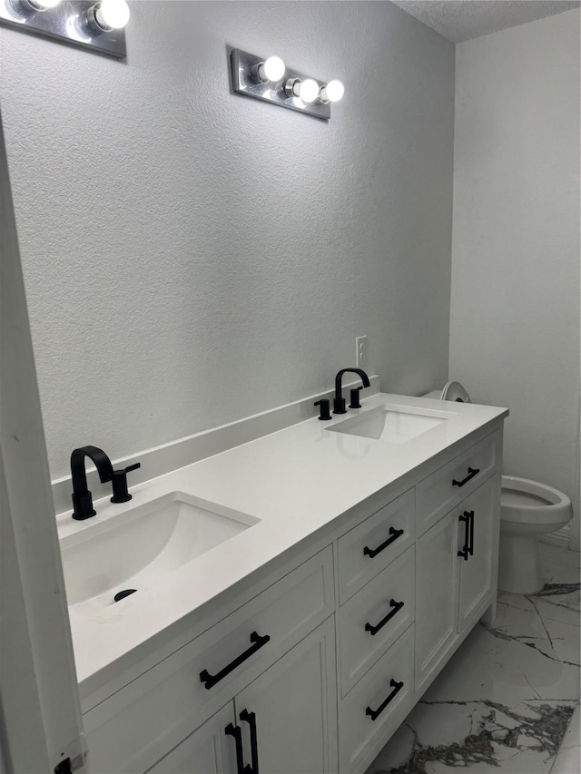 bathroom featuring double vanity, marble finish floor, toilet, and a sink