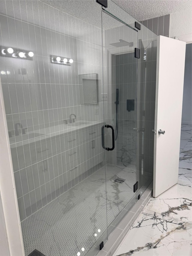 bathroom featuring marble finish floor, a shower stall, and a textured ceiling