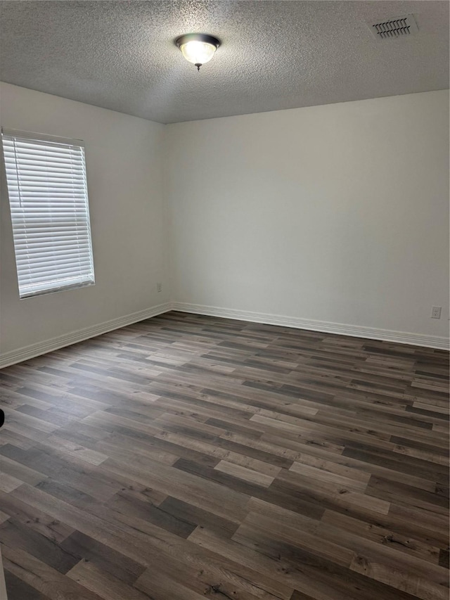 spare room with dark wood-style flooring, visible vents, a textured ceiling, and baseboards