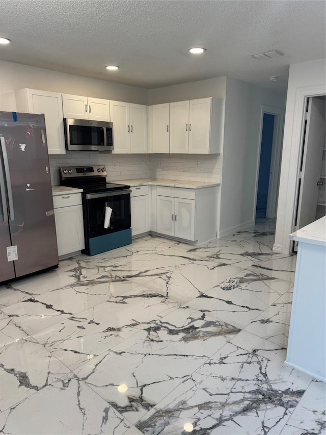 kitchen featuring a textured ceiling, white cabinetry, light countertops, appliances with stainless steel finishes, and backsplash