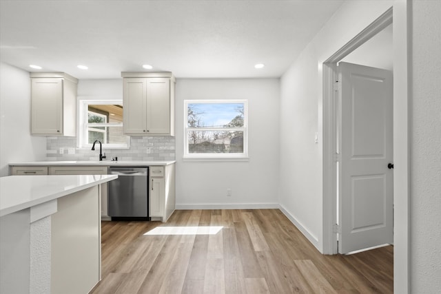 kitchen featuring baseboards, light countertops, light wood-style floors, stainless steel dishwasher, and backsplash