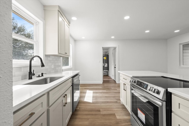 kitchen featuring recessed lighting, a sink, stainless steel appliances, light wood-style floors, and backsplash