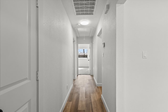 corridor with wood finished floors, visible vents, baseboards, attic access, and a textured wall