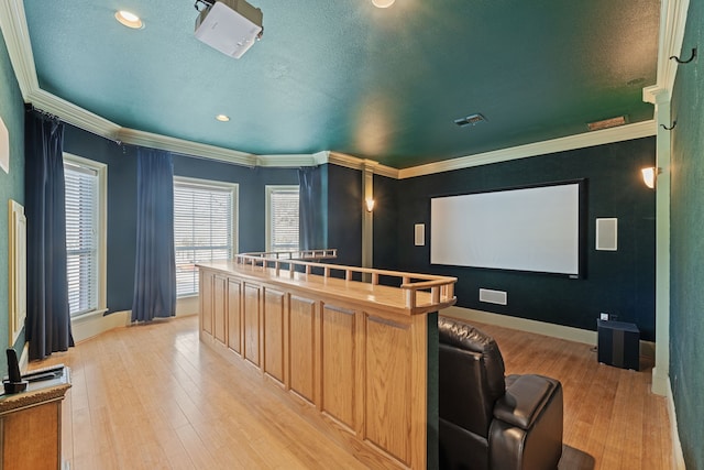 cinema featuring a textured ceiling, ornamental molding, light wood-style flooring, and baseboards