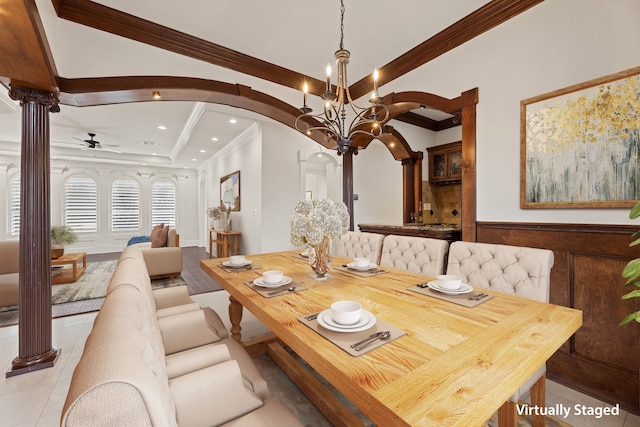 dining area with decorative columns, arched walkways, a wainscoted wall, ornamental molding, and ceiling fan with notable chandelier