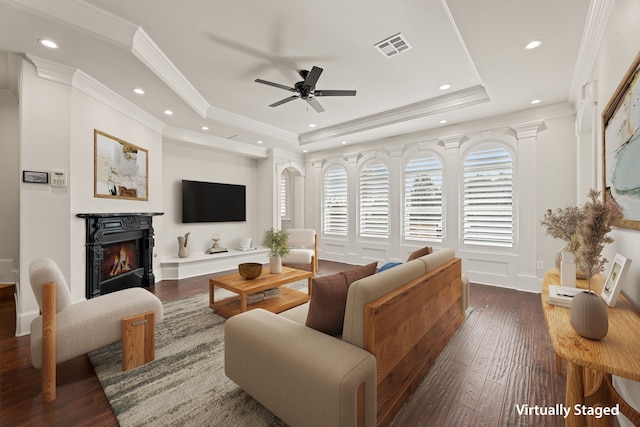 living room featuring dark wood-style flooring, visible vents, a ceiling fan, a raised ceiling, and a glass covered fireplace