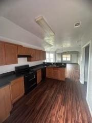 kitchen featuring dark countertops, brown cabinets, dark wood-type flooring, black gas stove, and under cabinet range hood