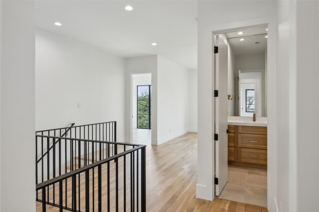 hallway featuring recessed lighting, baseboards, light wood finished floors, and an upstairs landing