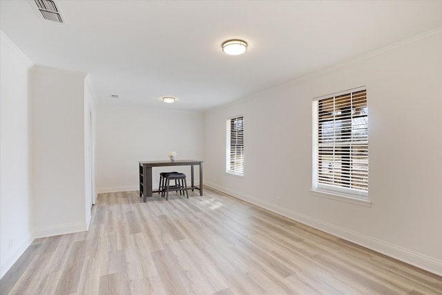 empty room with light wood-style flooring, visible vents, baseboards, and ornamental molding