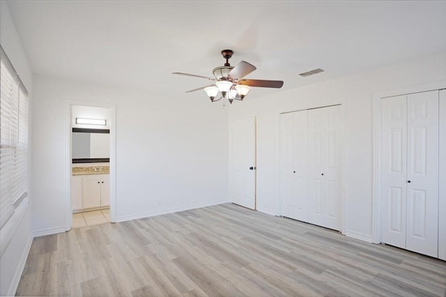 unfurnished bedroom with multiple closets, visible vents, ensuite bathroom, light wood-style floors, and baseboards