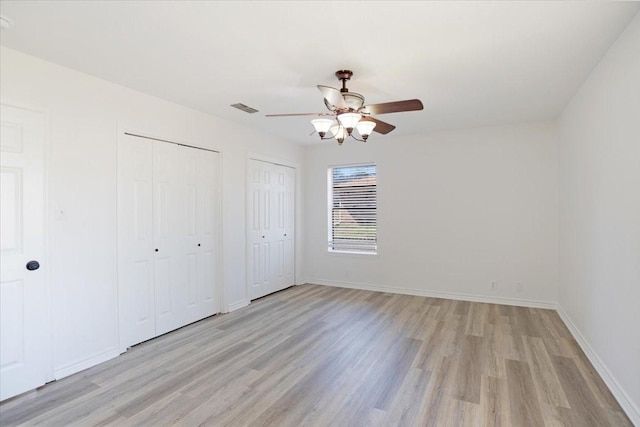 unfurnished bedroom featuring light wood-type flooring, baseboards, visible vents, and two closets