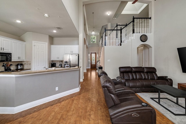 living room featuring light wood-type flooring, arched walkways, stairway, and baseboards