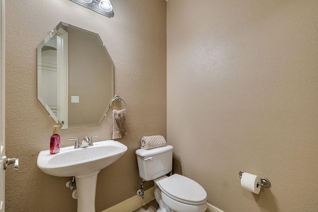 half bath featuring toilet, baseboards, and a sink