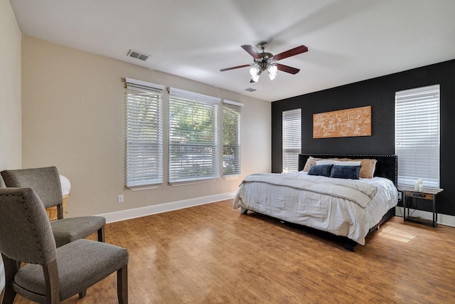 bedroom with a ceiling fan, light wood-type flooring, visible vents, and baseboards