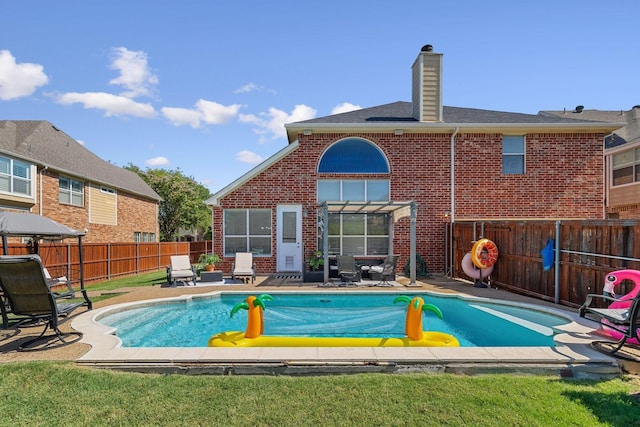 back of house with a fenced in pool, a fenced backyard, a chimney, a patio area, and brick siding