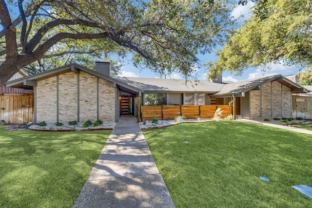 mid-century home featuring brick siding, a chimney, a front yard, and fence