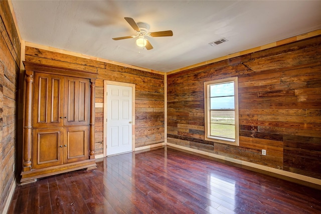unfurnished bedroom with dark wood-style floors, visible vents, wood walls, and ceiling fan