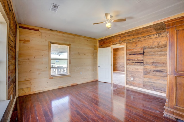 unfurnished room with dark wood-style floors, ceiling fan, visible vents, and wooden walls