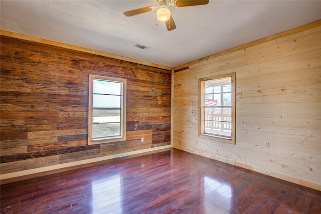 spare room featuring ceiling fan, dark wood-type flooring, visible vents, and wooden walls