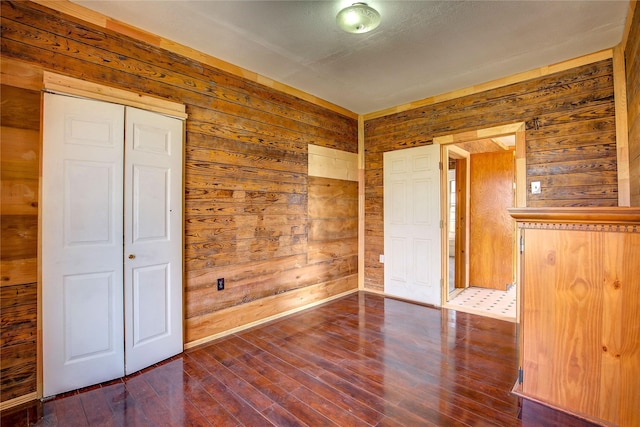 empty room featuring dark wood-style floors, baseboards, and wooden walls