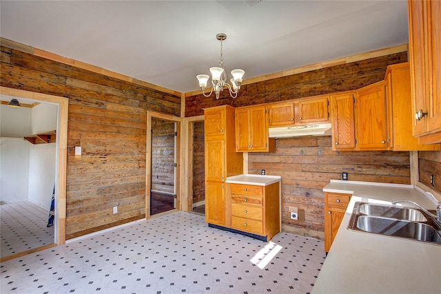 kitchen featuring light countertops, under cabinet range hood, a chandelier, pendant lighting, and a sink