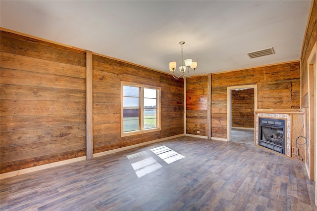 unfurnished living room with wooden walls, visible vents, wood finished floors, a fireplace, and a notable chandelier