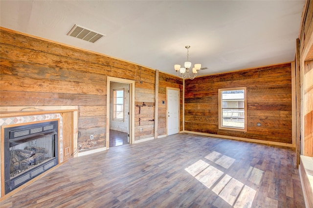 unfurnished living room with visible vents, wood finished floors, an inviting chandelier, wood walls, and a fireplace