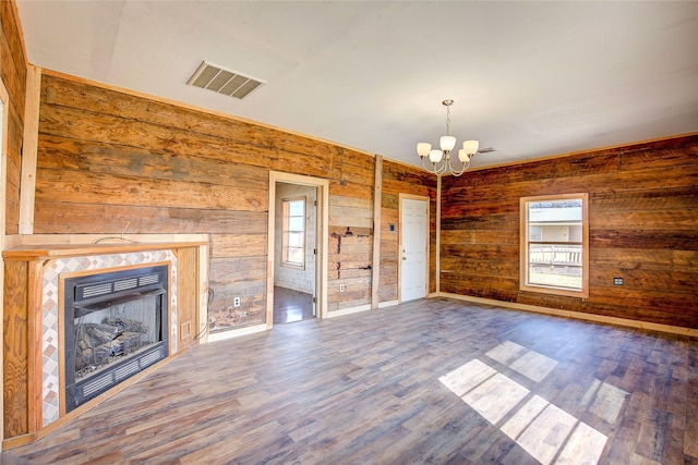 unfurnished living room featuring wooden walls, a notable chandelier, a fireplace, wood finished floors, and visible vents