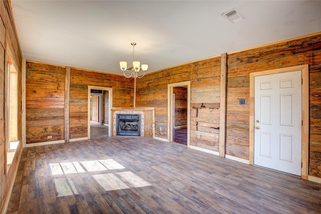 unfurnished living room with visible vents, wood finished floors, wood walls, a fireplace, and a chandelier