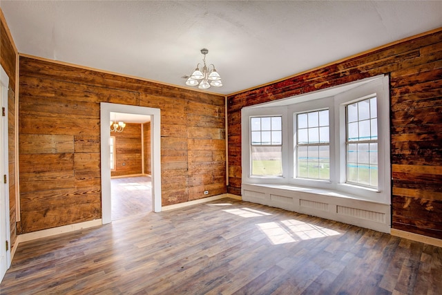 unfurnished room featuring baseboards, wood walls, wood finished floors, and an inviting chandelier