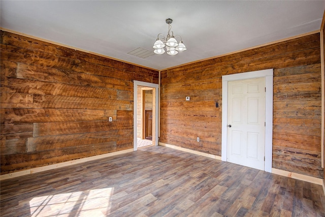unfurnished room featuring wood finished floors, wooden walls, baseboards, and an inviting chandelier
