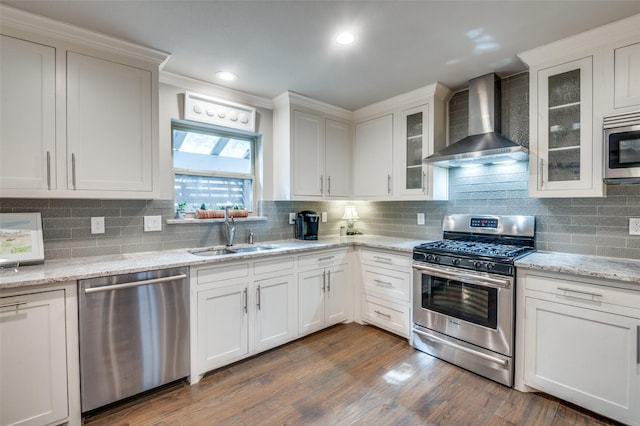 kitchen with stainless steel appliances, dark wood-type flooring, white cabinetry, a sink, and wall chimney exhaust hood